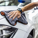 Mann reinigt Auto mit einen grauen Tuch